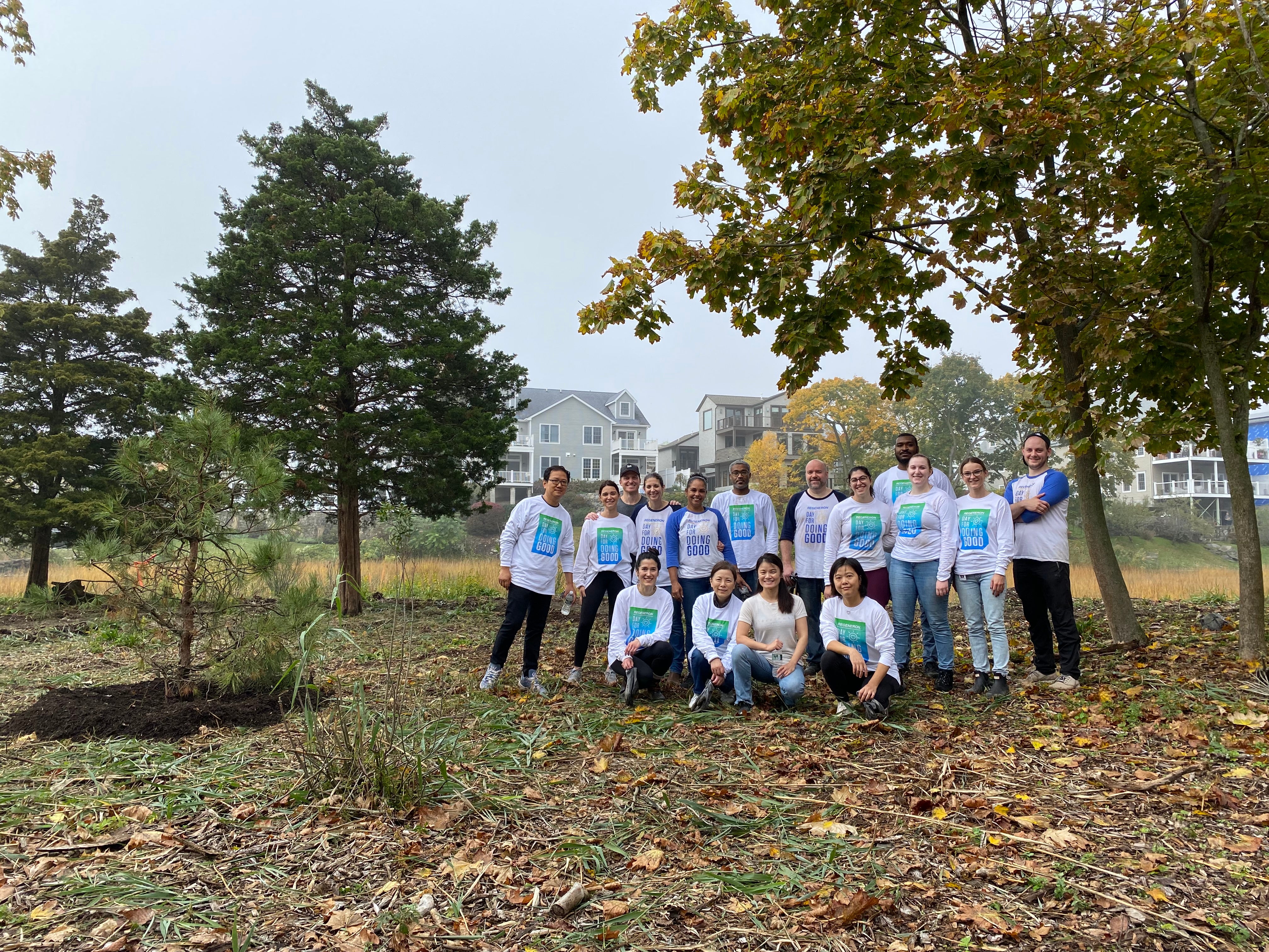 A group of volunteers in matching shirts pose at a restoration site with freshly planted trees.